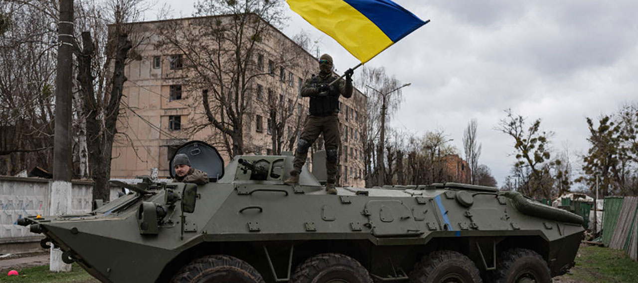 A soldier standing on top of a tank and waving a Ukrainian flag.