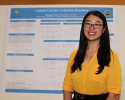 A student standing with their poster during the REU poster session.