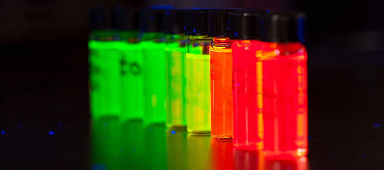 Vials of nano crystals fluoresce under UV light in a lab.