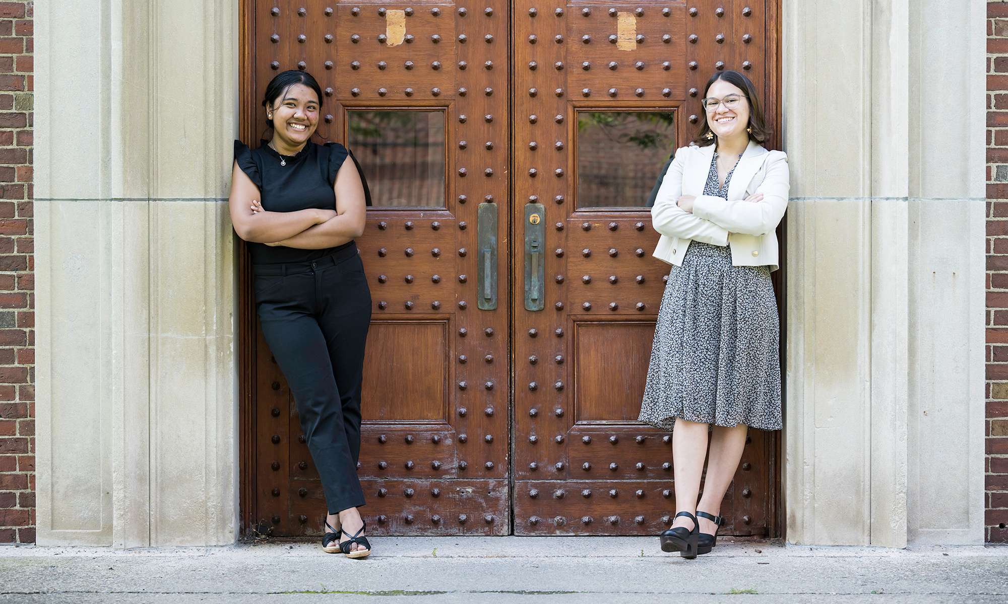 Mara Criollo-Rivera and Kristel Kezia Sagabaen Layugan smile as they pose for a photo leaning against the doors of Rush Rhees Library.