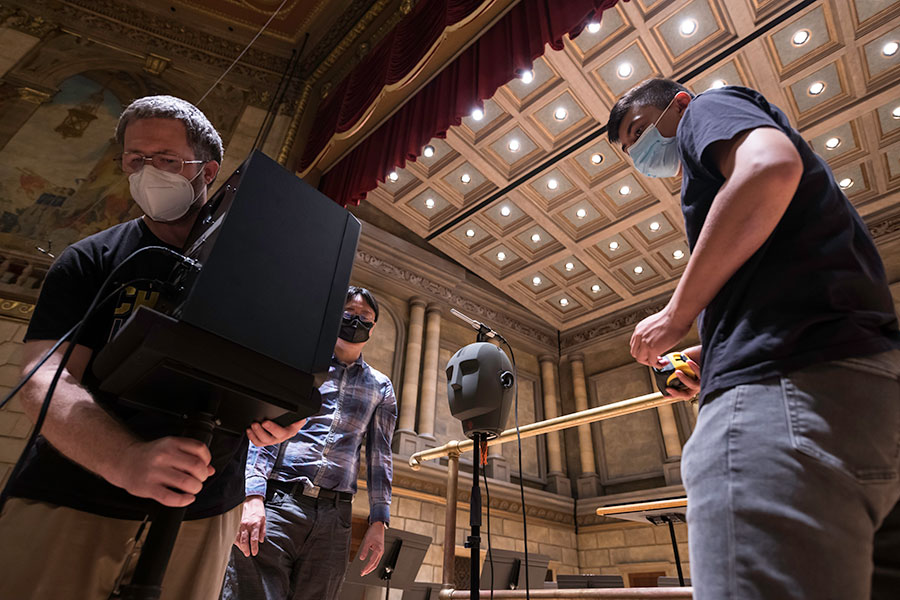 A professor and students reposition a speaker used in the audio data gathering process on the Kodak Hall stage.