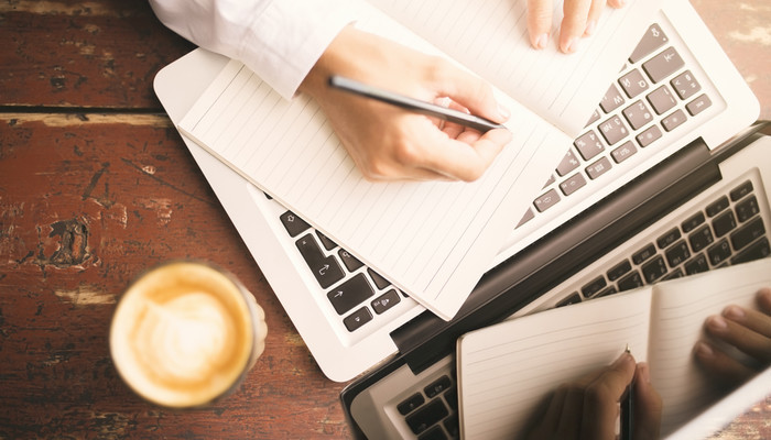 Image of person writing on paper near laptop