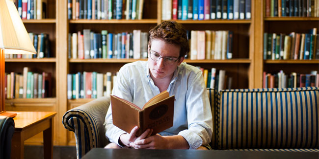 A student holding a book in front of a bookcase.