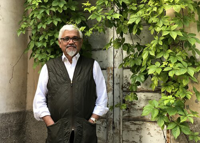 Amitav Ghosh standing in front of some foliage.