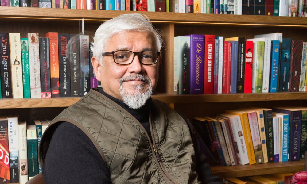 Amitav Ghosh in front of a bookshelf.