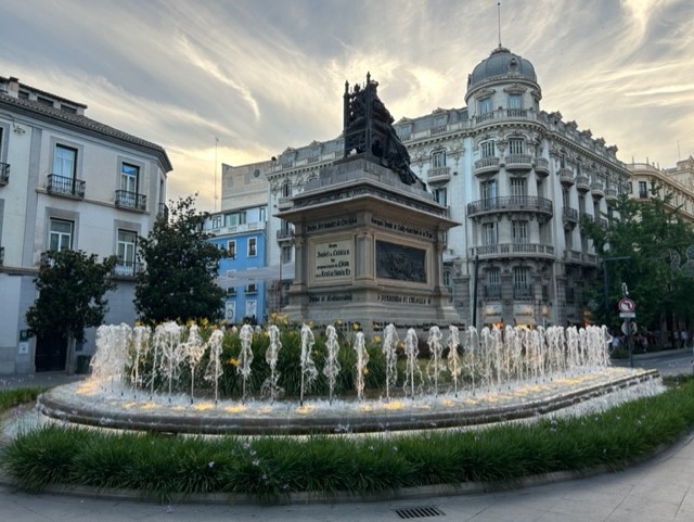 A statue in a town square surrounded by spraying fountains of water.