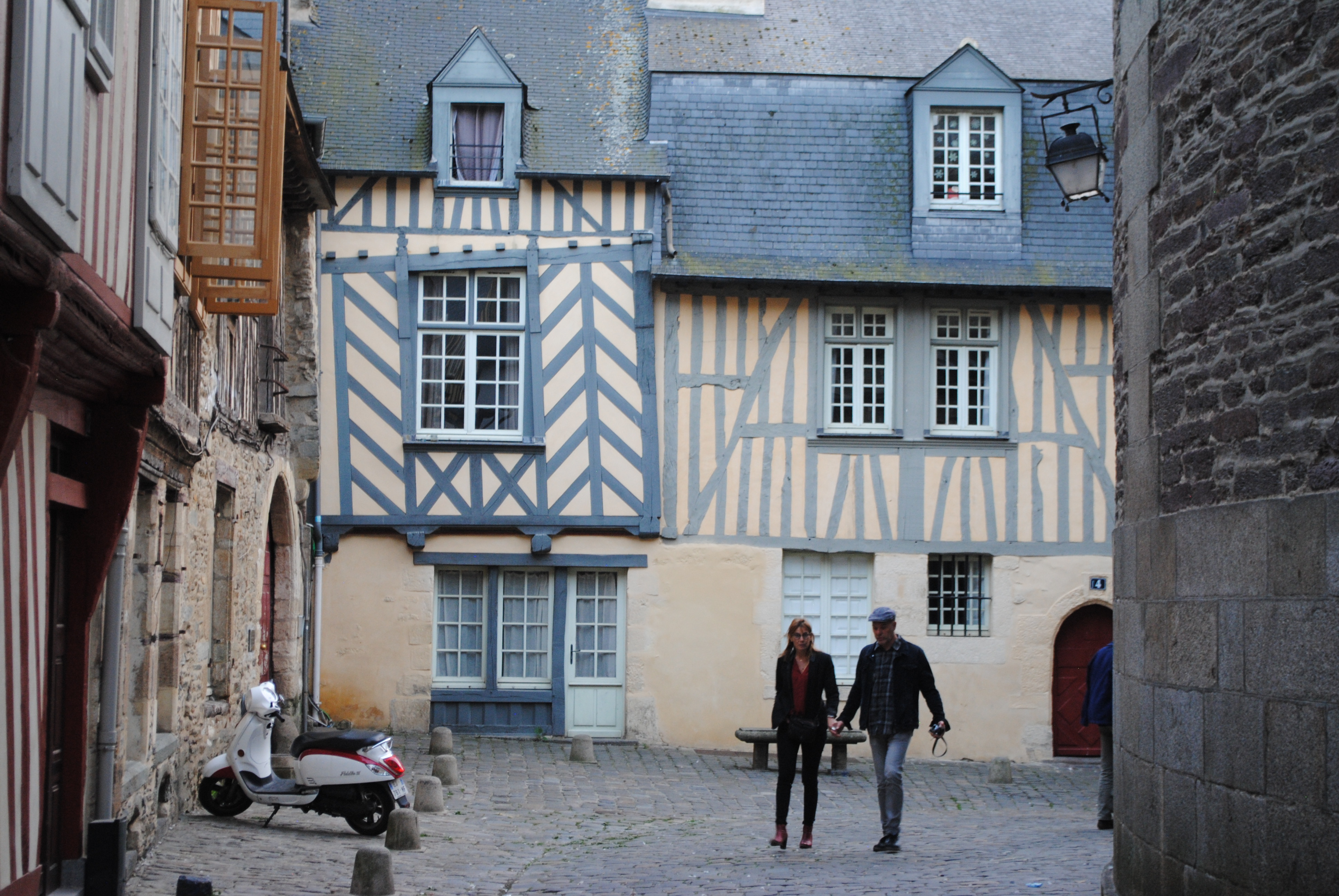 back corner of old houses with decorative blue woodwork on the sides and two people walking nearby