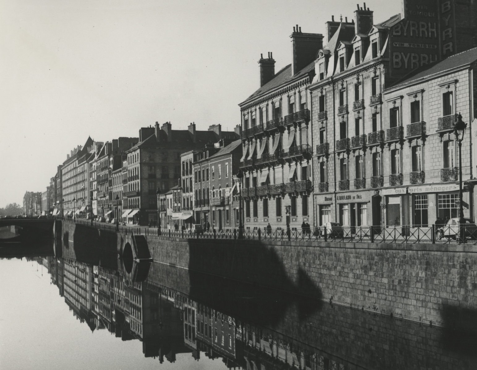 black and white photo of buildings stretch into distance on right, next to a river