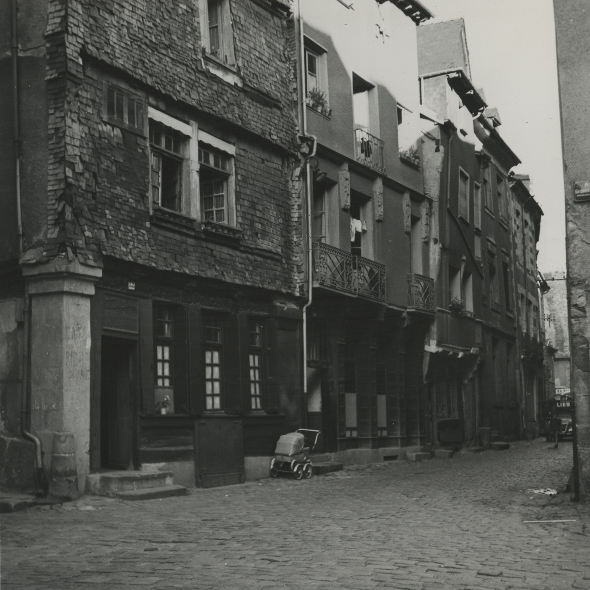 black and white photo of houses facing a narrow street, there is a baby carriage outside one of the houses