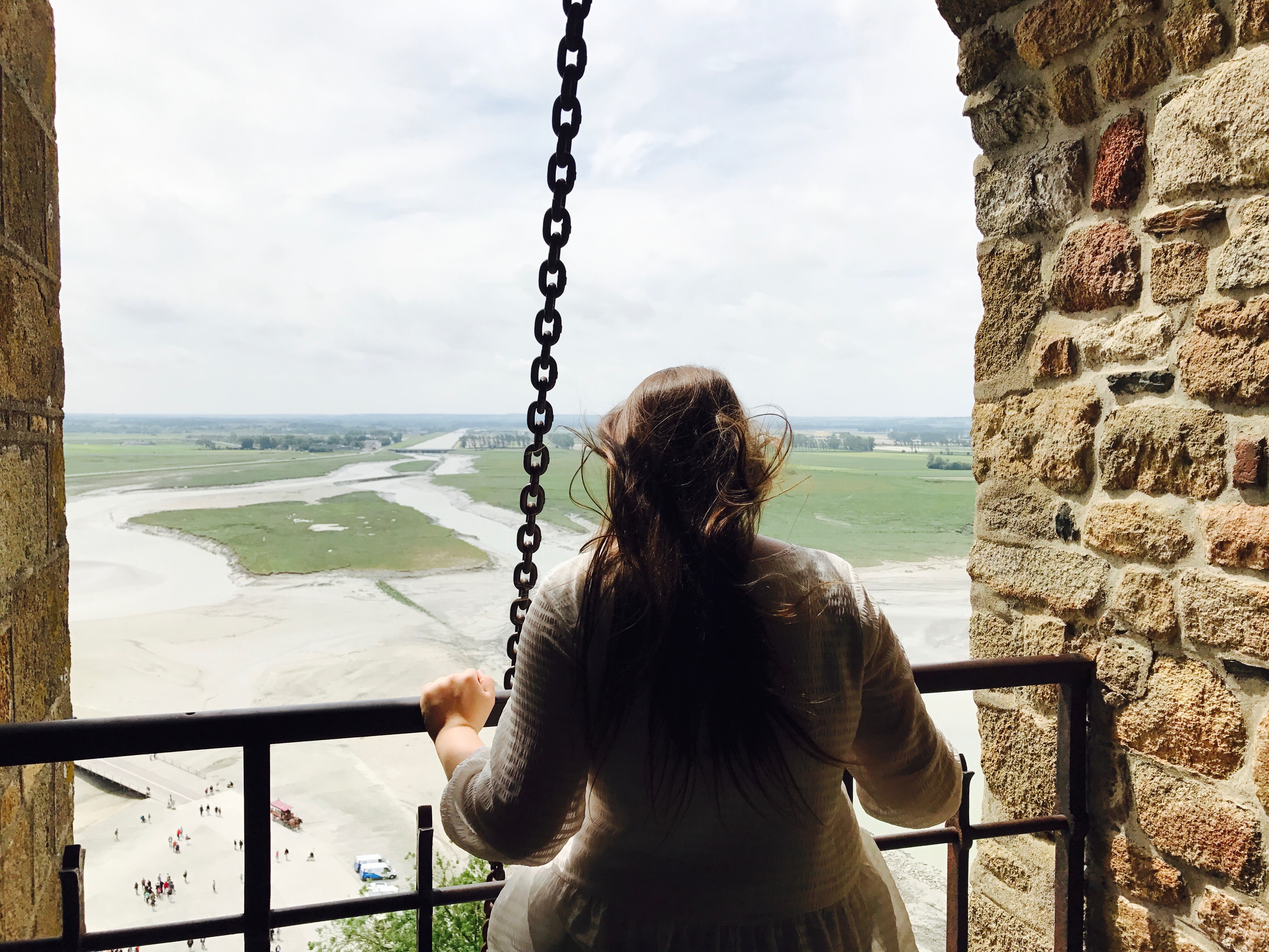 girl seen from behind looking over a balcony ledge at a green field