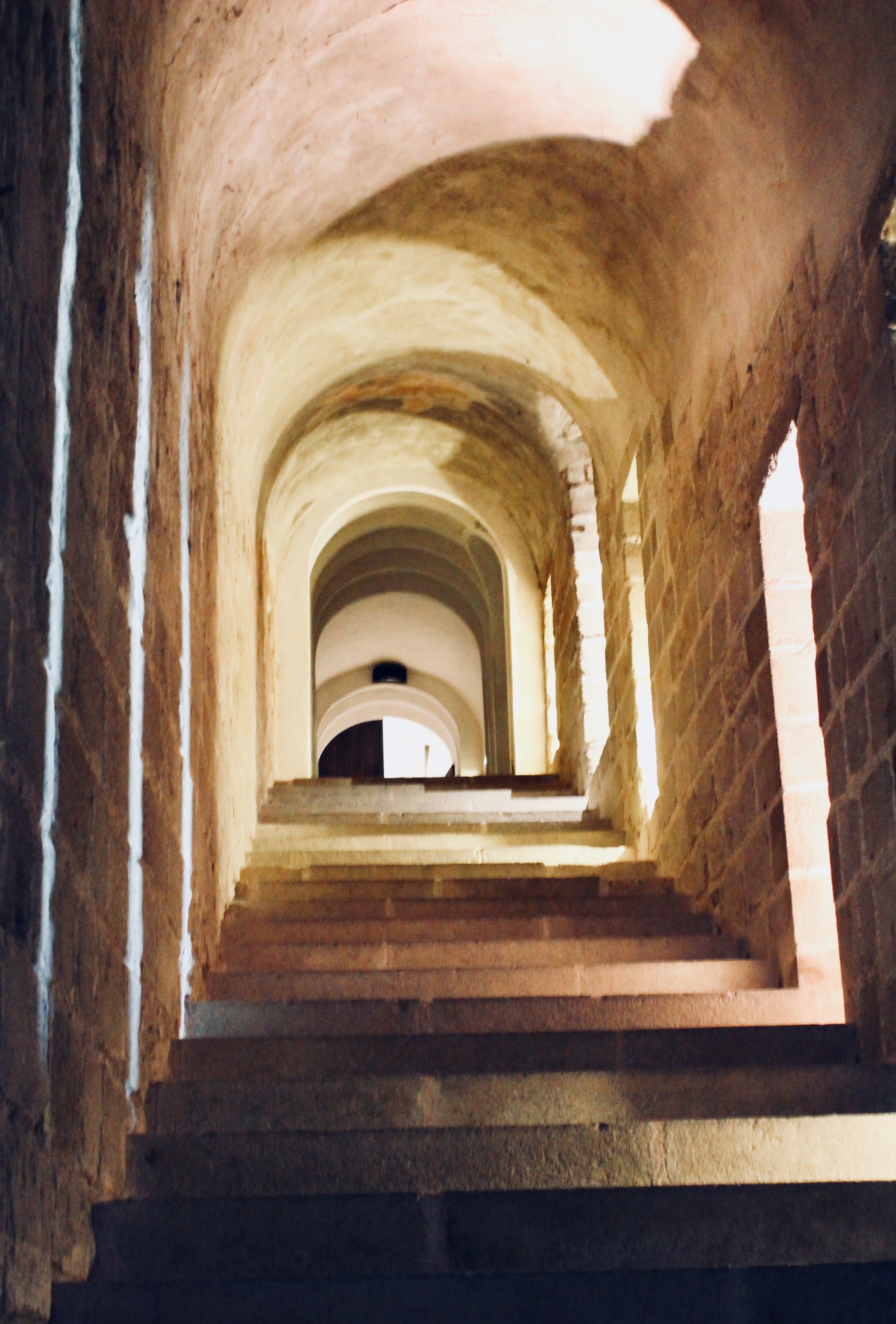 narrow stone staircase with arched ceiling and open windows on the right side