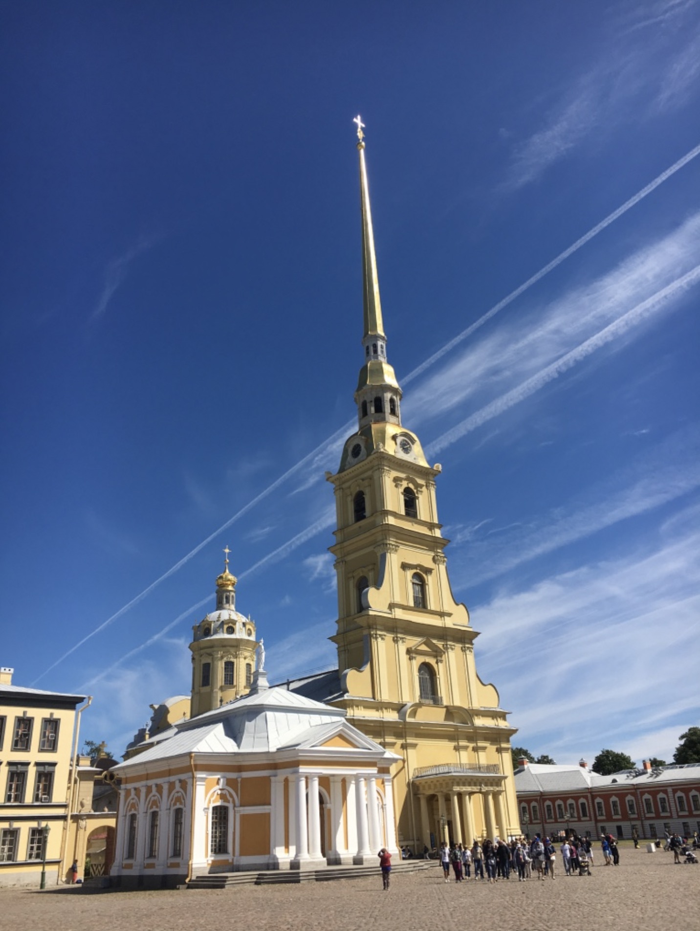 yellow building with tall tower and spire against blue sky with light clouds