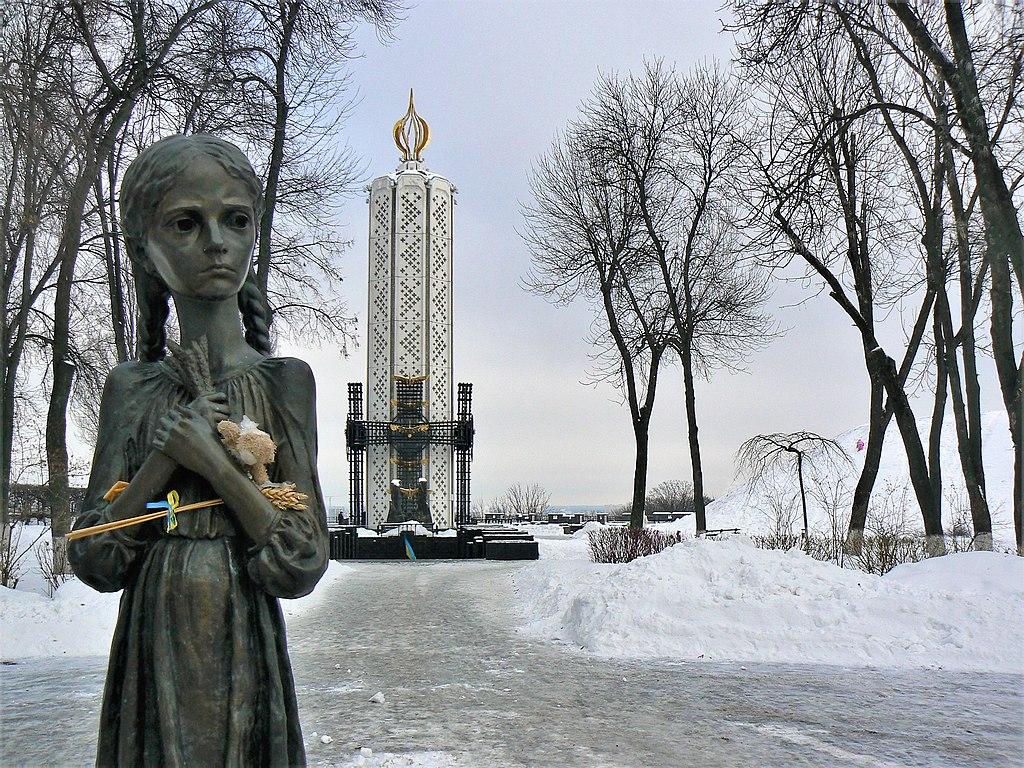 A statue of a famished young girl in front of a monument.