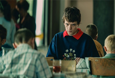 A young man in a cafeteria staring menacingly at others.