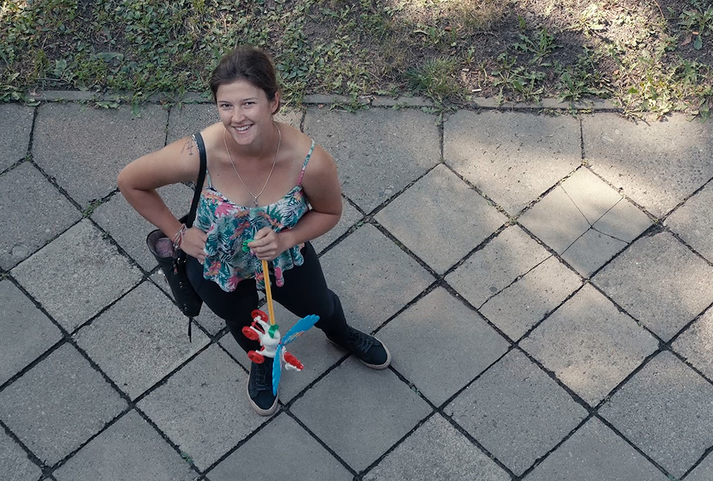 A still image from the movie of a woman standing on a sidewalk looking up and smiling at the camera.