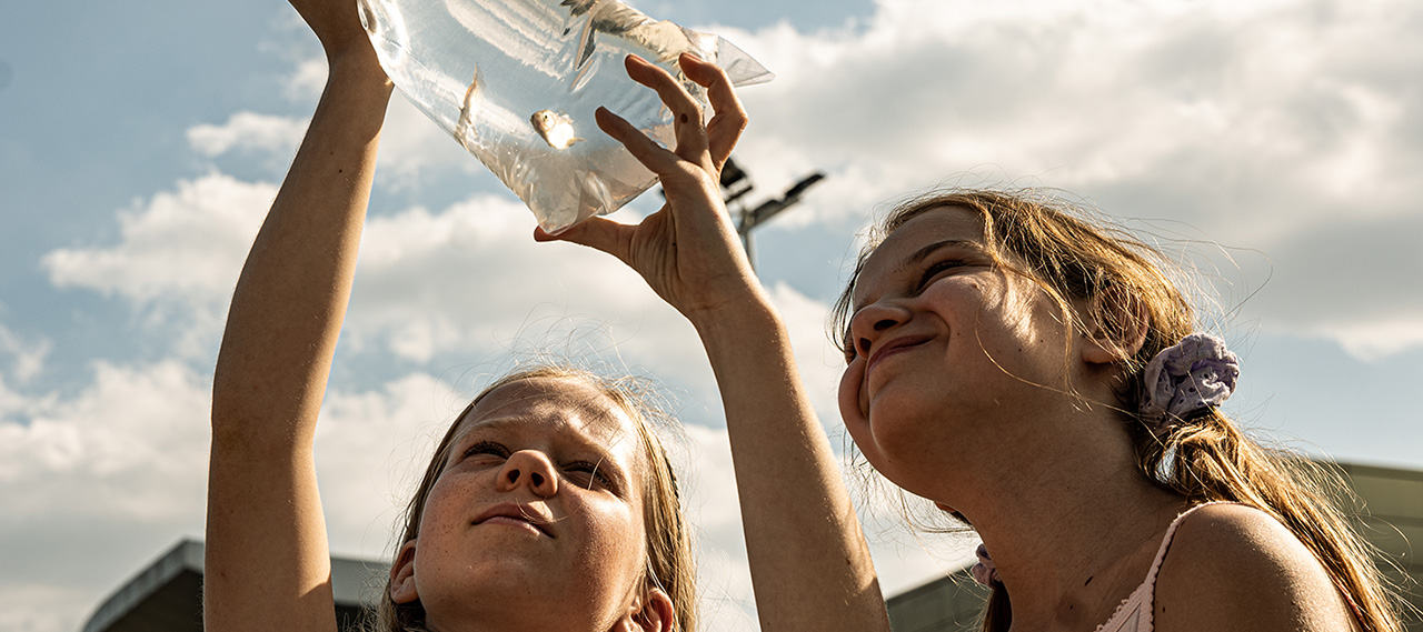 Two young girls holding a glass jar up to the sky.
