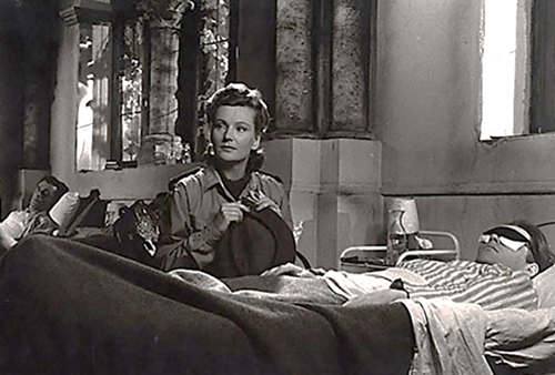 A still image from the movie of a woman sitting at the bedside of a patient in a hospital.