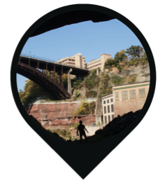 A graphic teardrop shape with a silhouetted person overlayed on an image of a building and bridge.