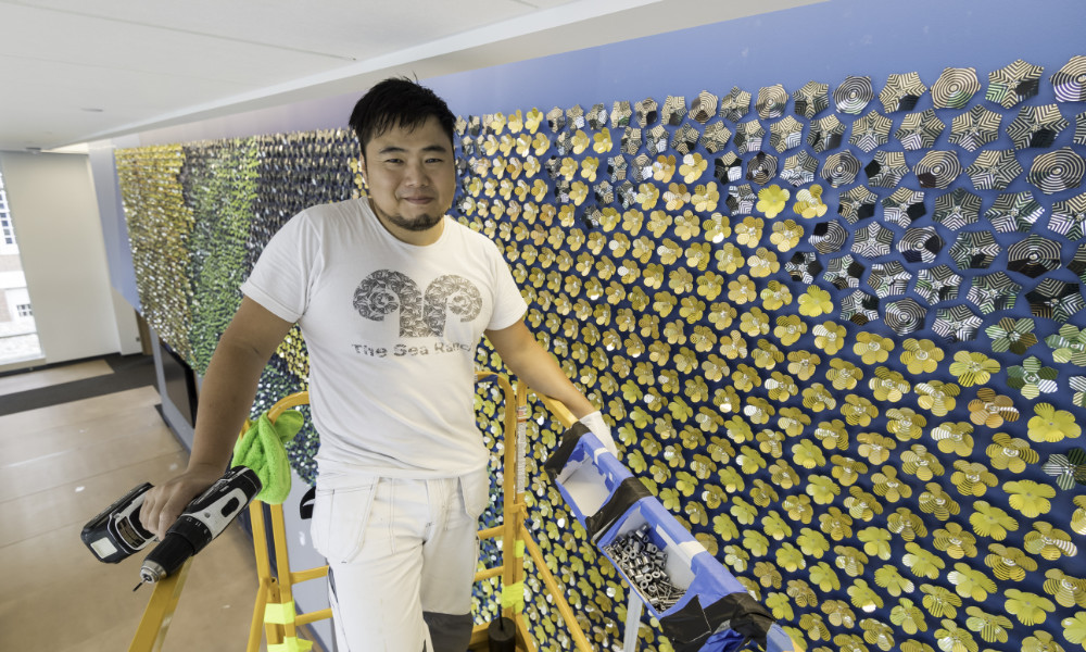 Artist Jay Yan poses for a photo as he installs a mosaic mural consisting of nearly 8,000 stainless steel pieces in the main entrance of the recently completed Sloan Performing Arts Center. (University of Rochester photo / J. Adam Fenster)