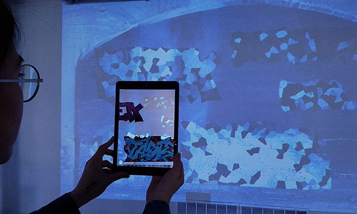 A student holds up an iPad to reveal graffiti from the Rochester Subway hidden in projected images.