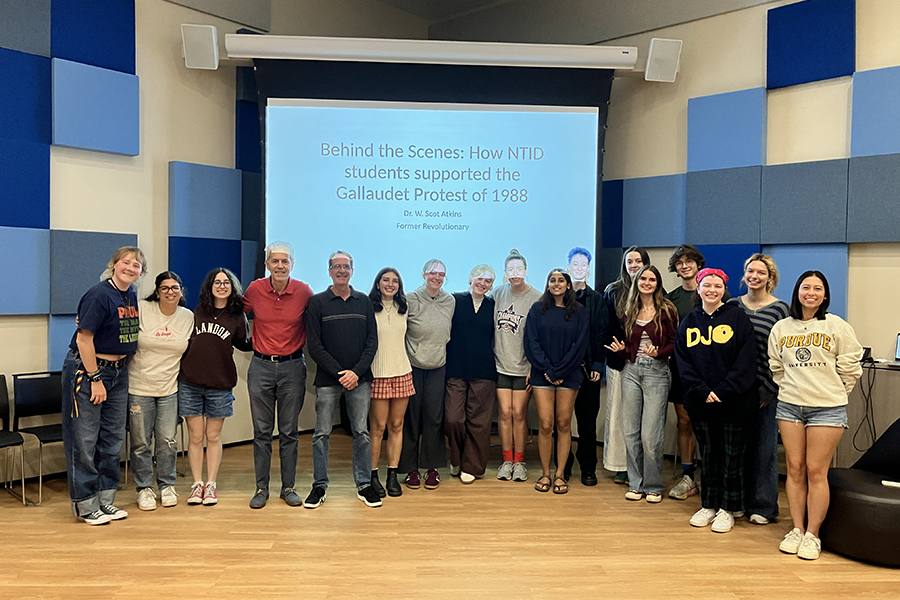 A large group of people pose in front of a projection screen.