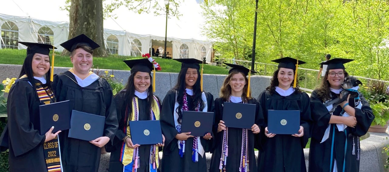 A group of ASL graduates from the class of 2022 posing for a photo on the Hajim Quad with their diplomas.