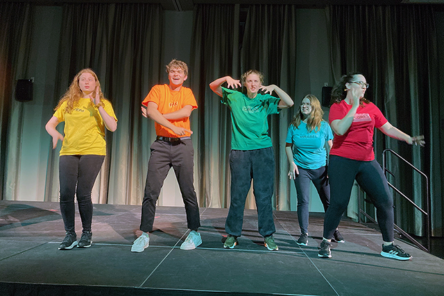 A group performs on stage with pink lighting.