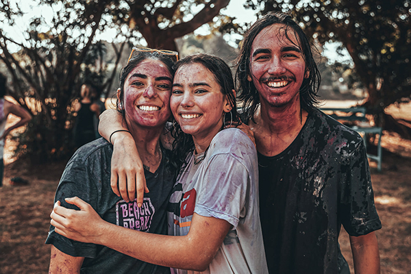 Three people covered in mud smiling at the camera.