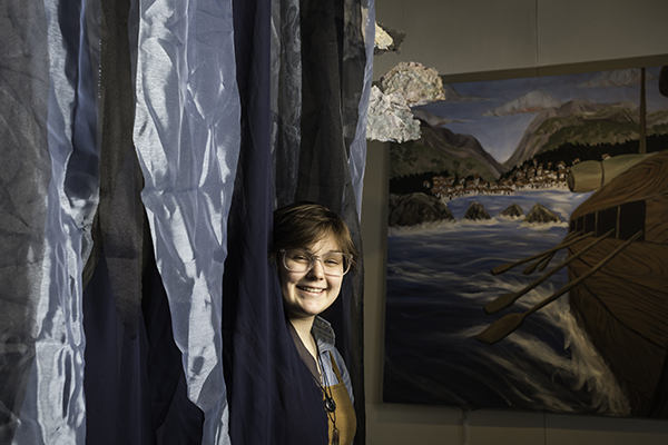 A student is shown peaking around their artwork in the gallery.