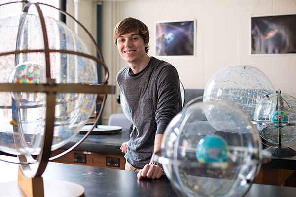 A student standing behind a desk with globes on it.