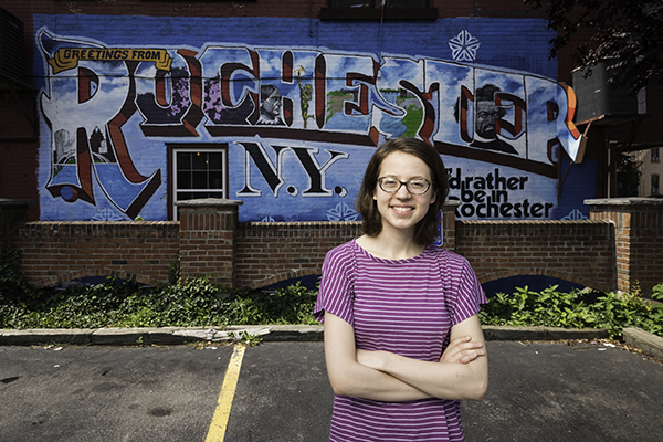 A student stands in front of a mural with their arms crossed.