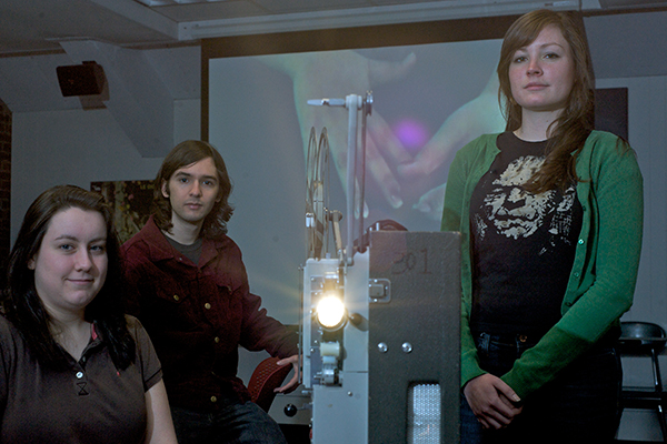 Three winners of a past Gollin Film Festival are shown in a darkened room with a projector.