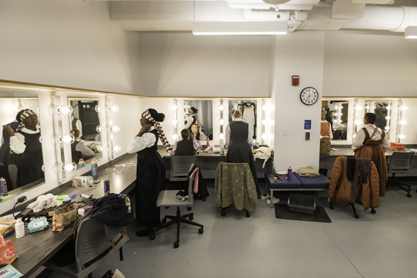 Actors in front of mirrors in a dressing room making last minute adjustments to their costumes.