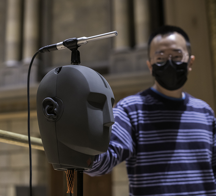 Binaural dummy head, used to simulate how human hearing works is seen on the stage in Kodak Hall alongside a student.
