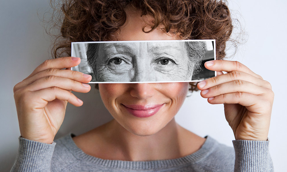A young women holding a photo of her aged over her eyes.