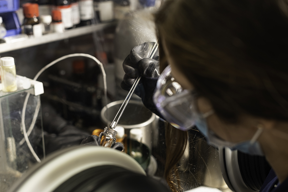 A student seen from behind dropping a capsule into a beaker.