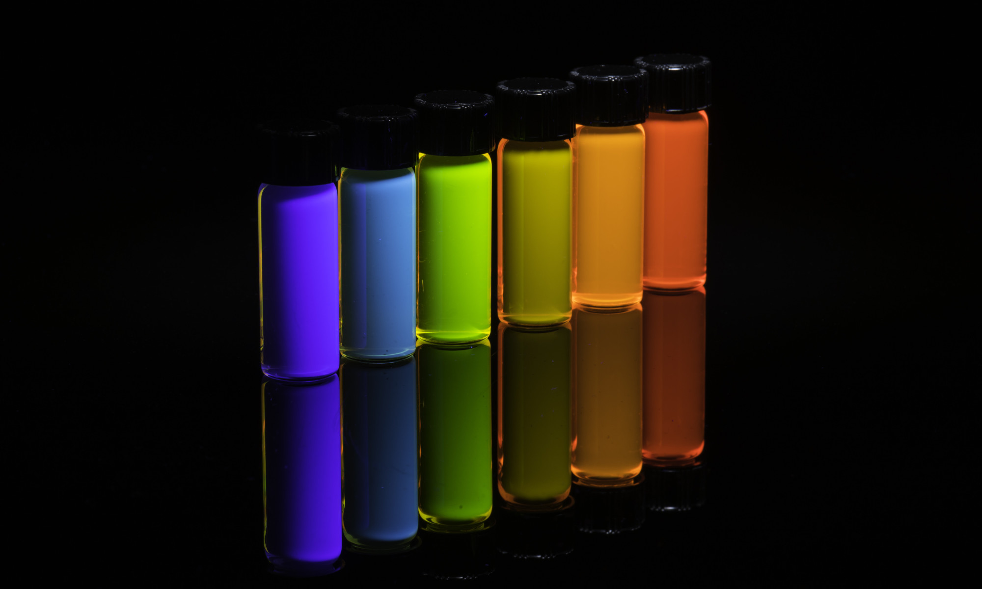 Six vials of quantum dots fluoresce in bright colors against a black background.