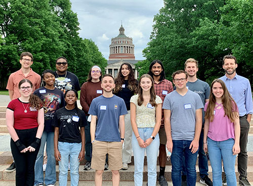 REU class of 2022 posing for a group photo on the Eastman Quad with the tower of Rush Rhees library in the background.