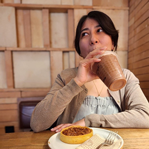 Daniela sipping a straw while seated at a table with a meal.
