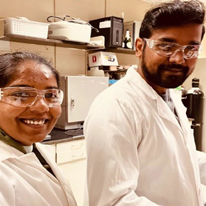 Lakshan and another person wearing safety glasses and white lab coats smile at the camera.