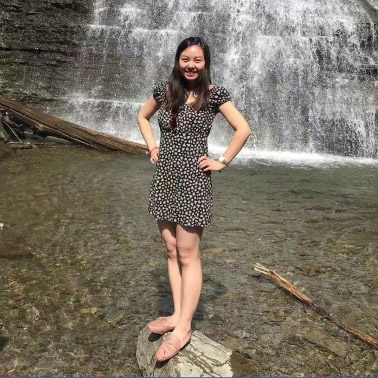 Yu standing on a rock outcropping at the base of a waterfall.