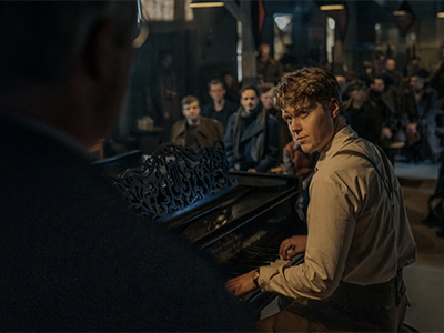 A still image from the film of a man playing a piano while a crowd watches.