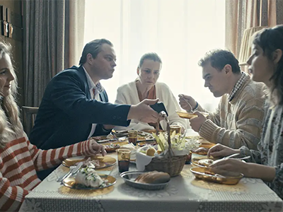 A still image from the film of a group of four adults having conversations at a dinner table.