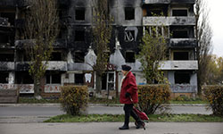 a Ukrainian civilian walking past a damaged building.