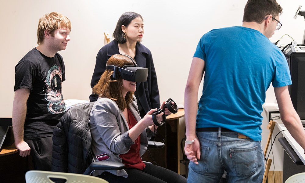 From left, A.J. Brown, Guan Zhewen, and David Backer look on as graduate student Helen Davies tries out clEAR, the virtual reality app they designed that allows users to better understand how to interact with people on the spectrum of hearing loss.