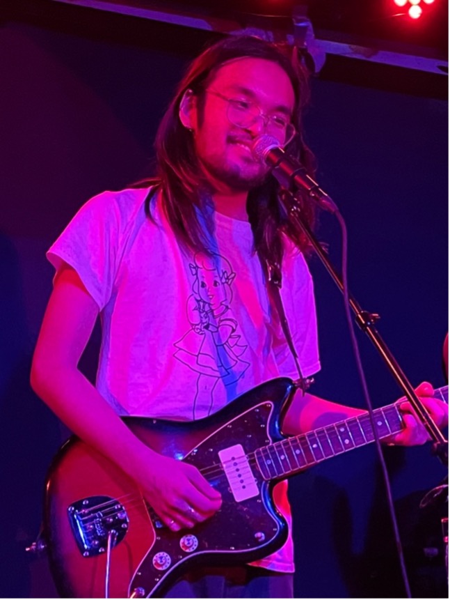 Ryohei Shima playing a guitar and singing into a micophone.