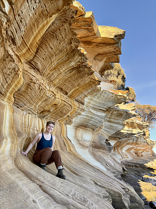Ren crouching on some rocks and smiling at the camera.