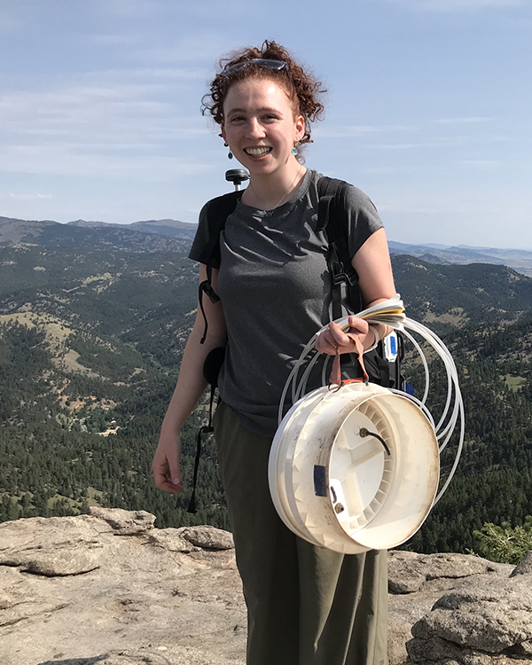 Maggie holding some equipment while standing on a mountain top.