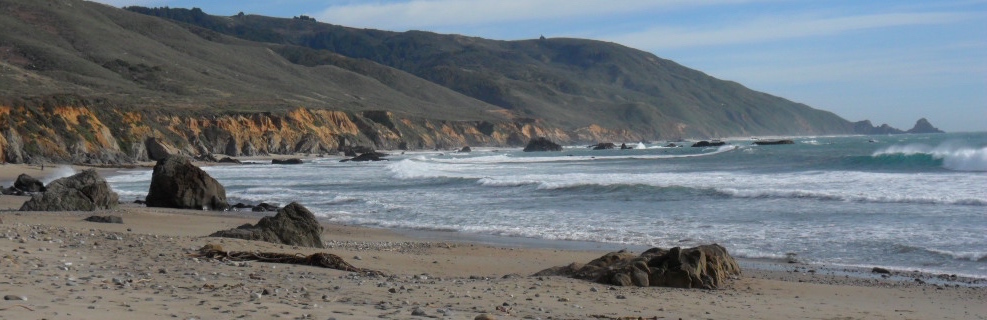 Waves coming ashore a beach with hills in the background.