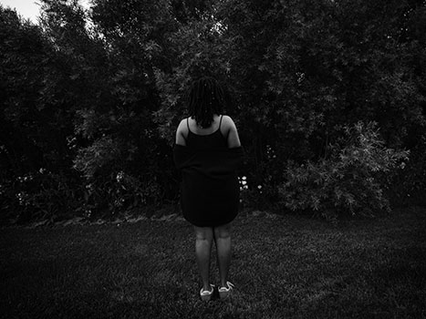 Alexandrai Brown in front of a hedge with her back to the camera.